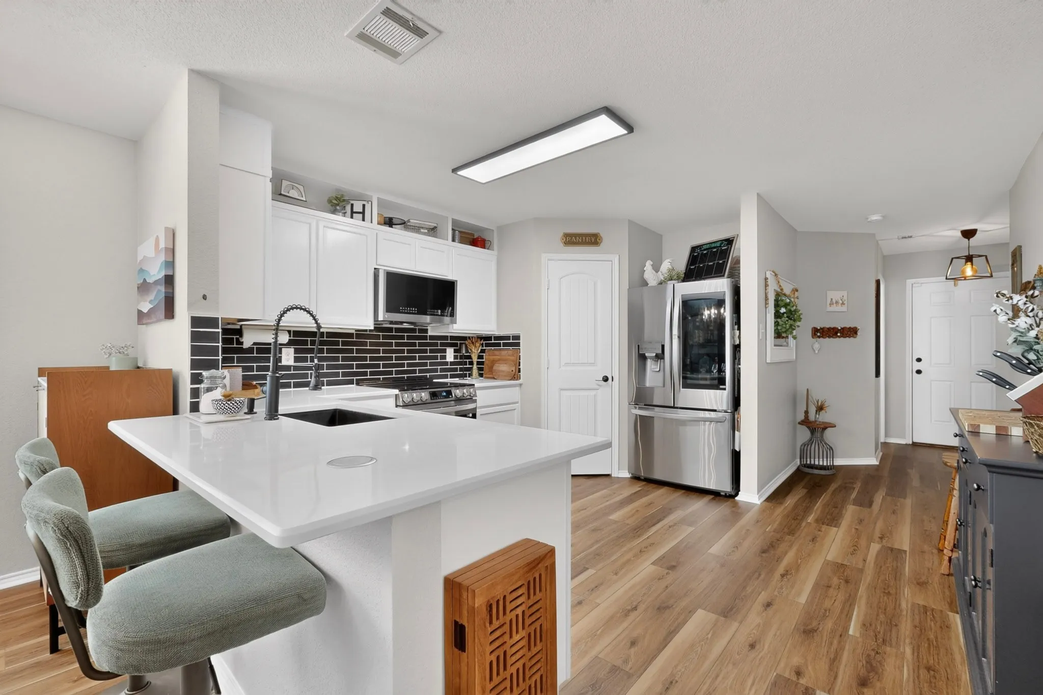 Kitchen featuring an island with a light-toned countertop, white cabinetry, black subway tile backsplash, and wood-finish flooring