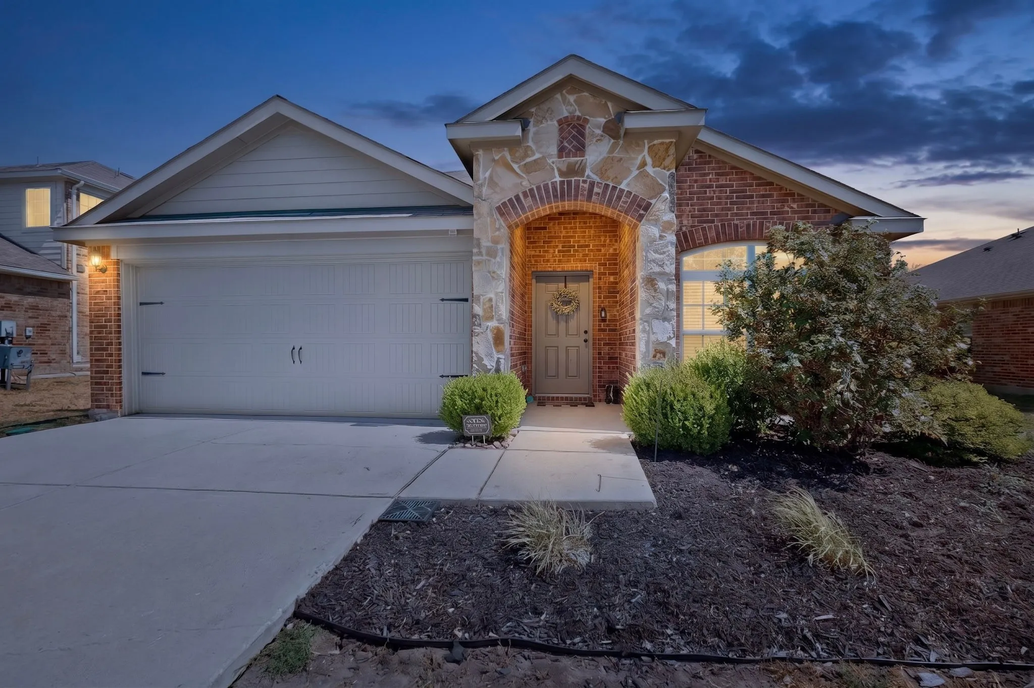Brick and stone facade with an arched entryway, attached garage, and concrete driveway
