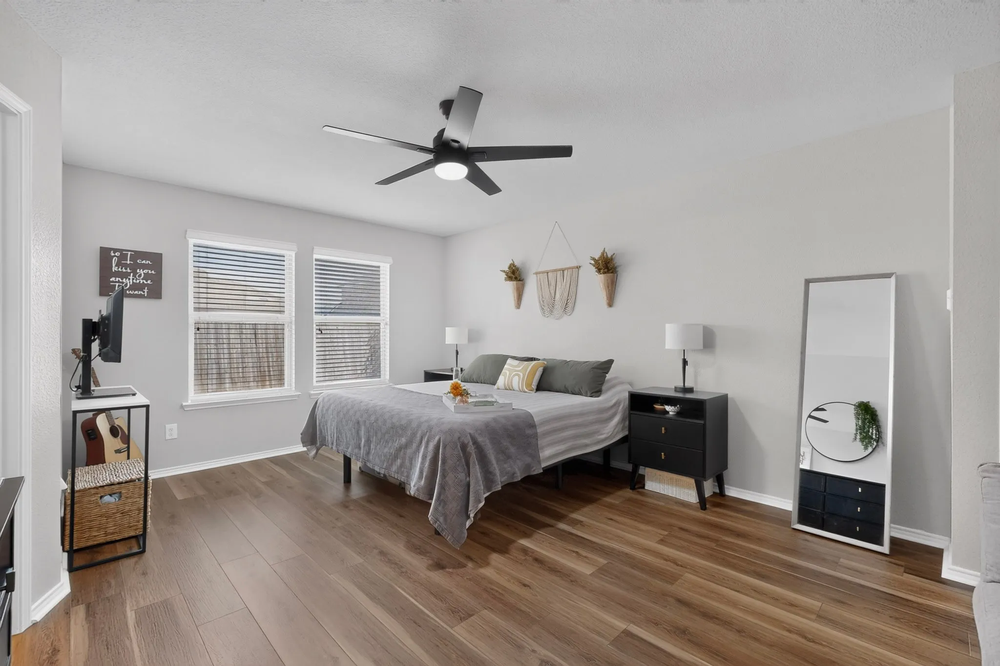 Wood-finish flooring, two windows with blinds, a ceiling fan with integrated lighting, and light gray wall paint