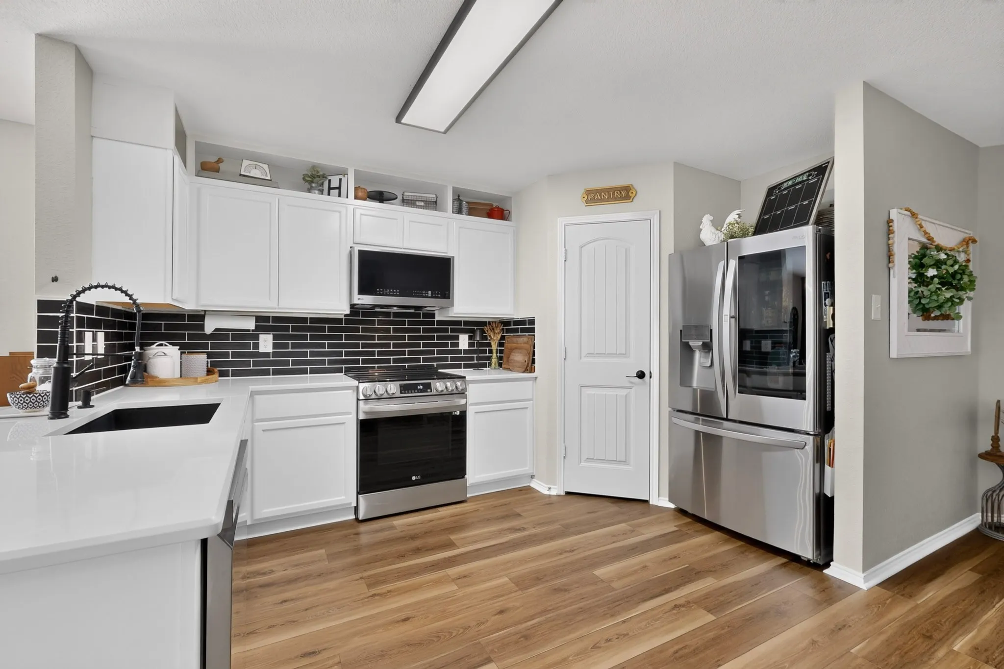 Kitchen featuring wood-finish flooring, white cabinetry, a black subway tile backsplash, white countertops, and stainless steel appliances