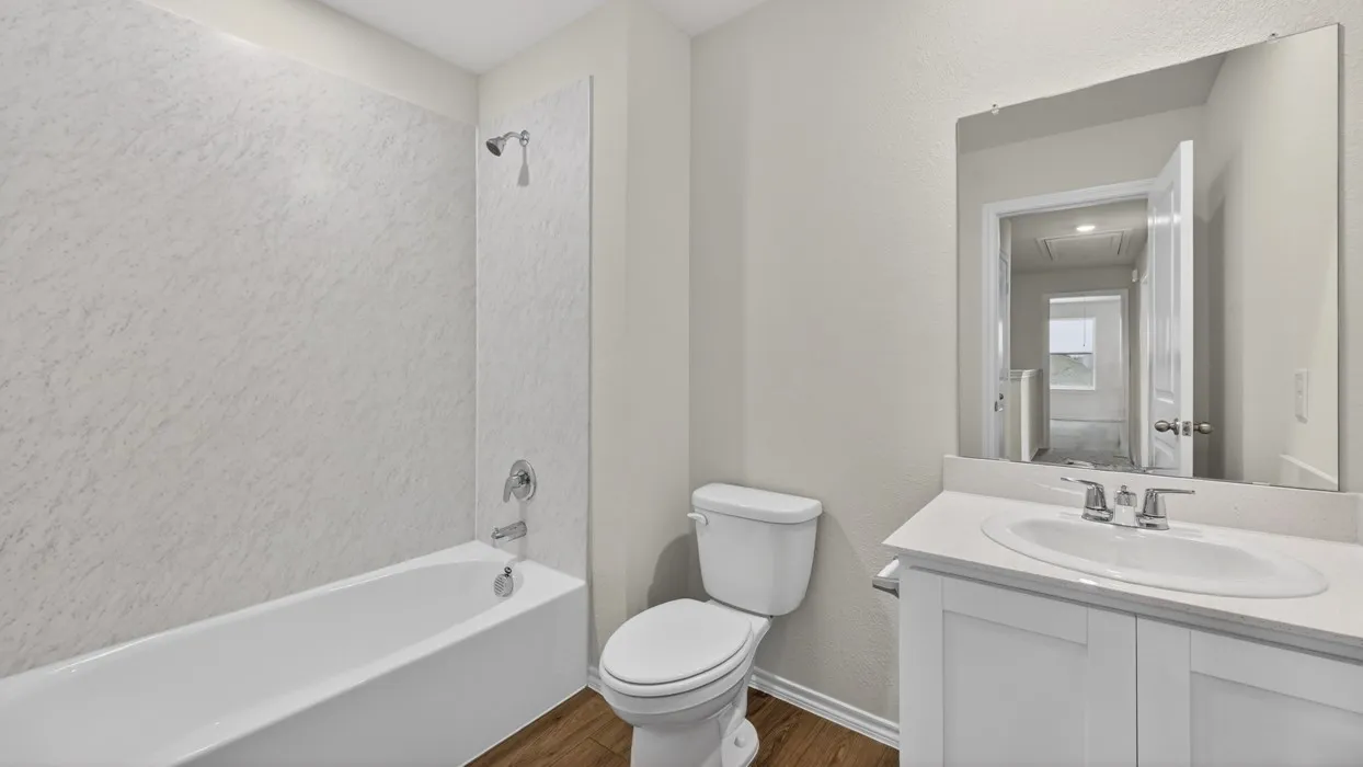 Tub-shower combination with white surround, single-basin vanity with a light-toned countertop, chrome fixtures, and wood-finish flooring