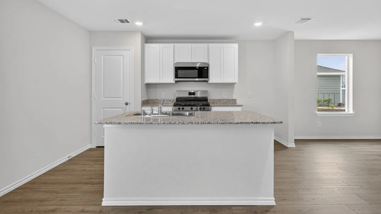 Kitchen island with integrated sink, white cabinetry, stainless steel appliances, wood-finish flooring, and light-colored countertops