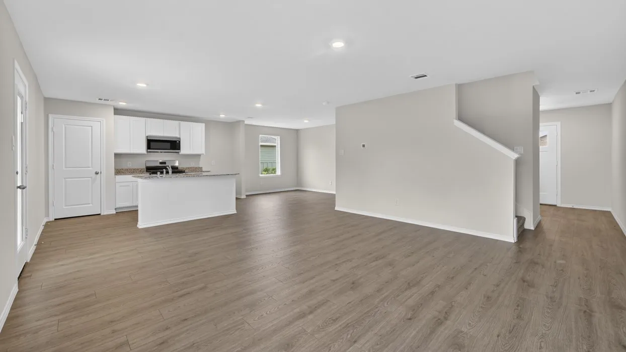 Open-concept living area with wood-finish flooring, recessed lighting, and a kitchen featuring white cabinetry, a kitchen island, and a stainless steel microwave