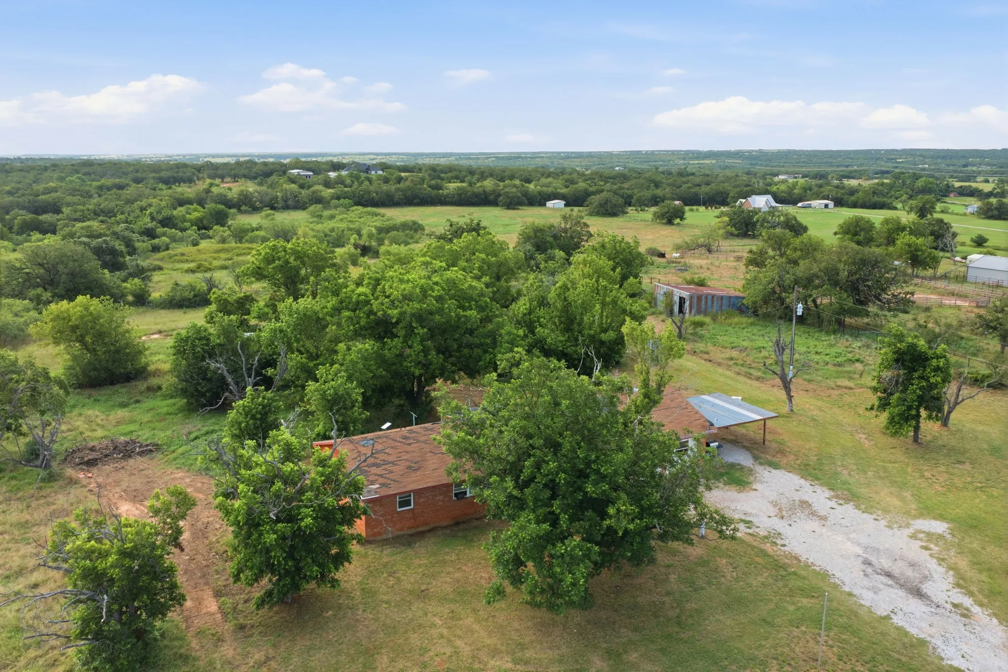 Expansive rural property featuring a brick residence nestled among mature shade trees, with manicured grounds extending across multiple acres