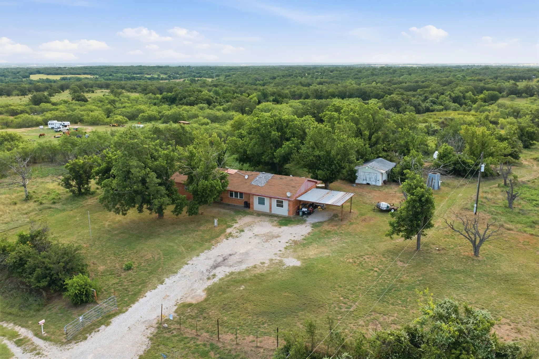 Expansive natural landscape surrounding a residence with a covered patio, a detached shed, and a gravel driveway
