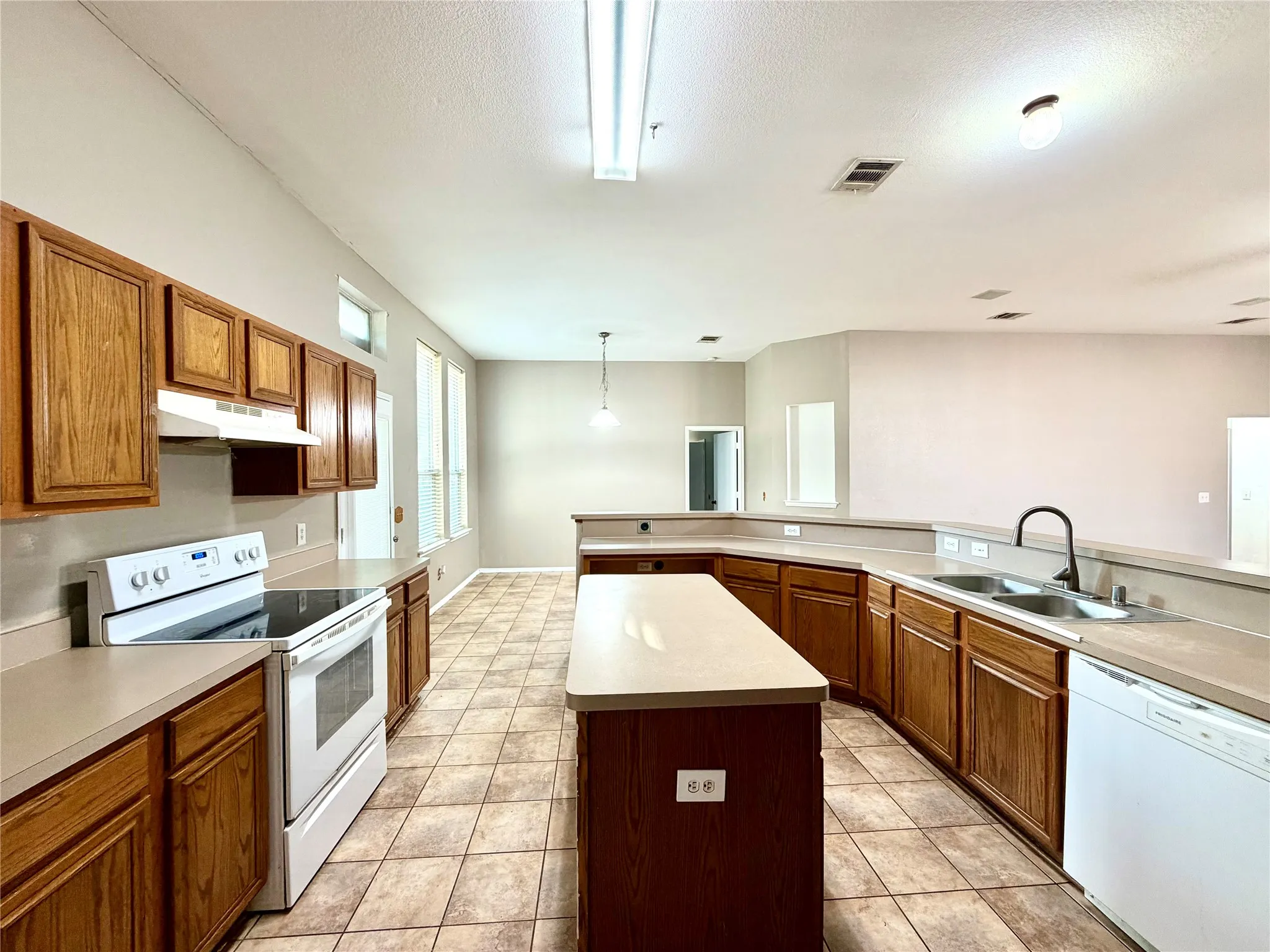 Kitchen featuring wood cabinetry, a center island, tile flooring, a dual basin sink, and a white electric range