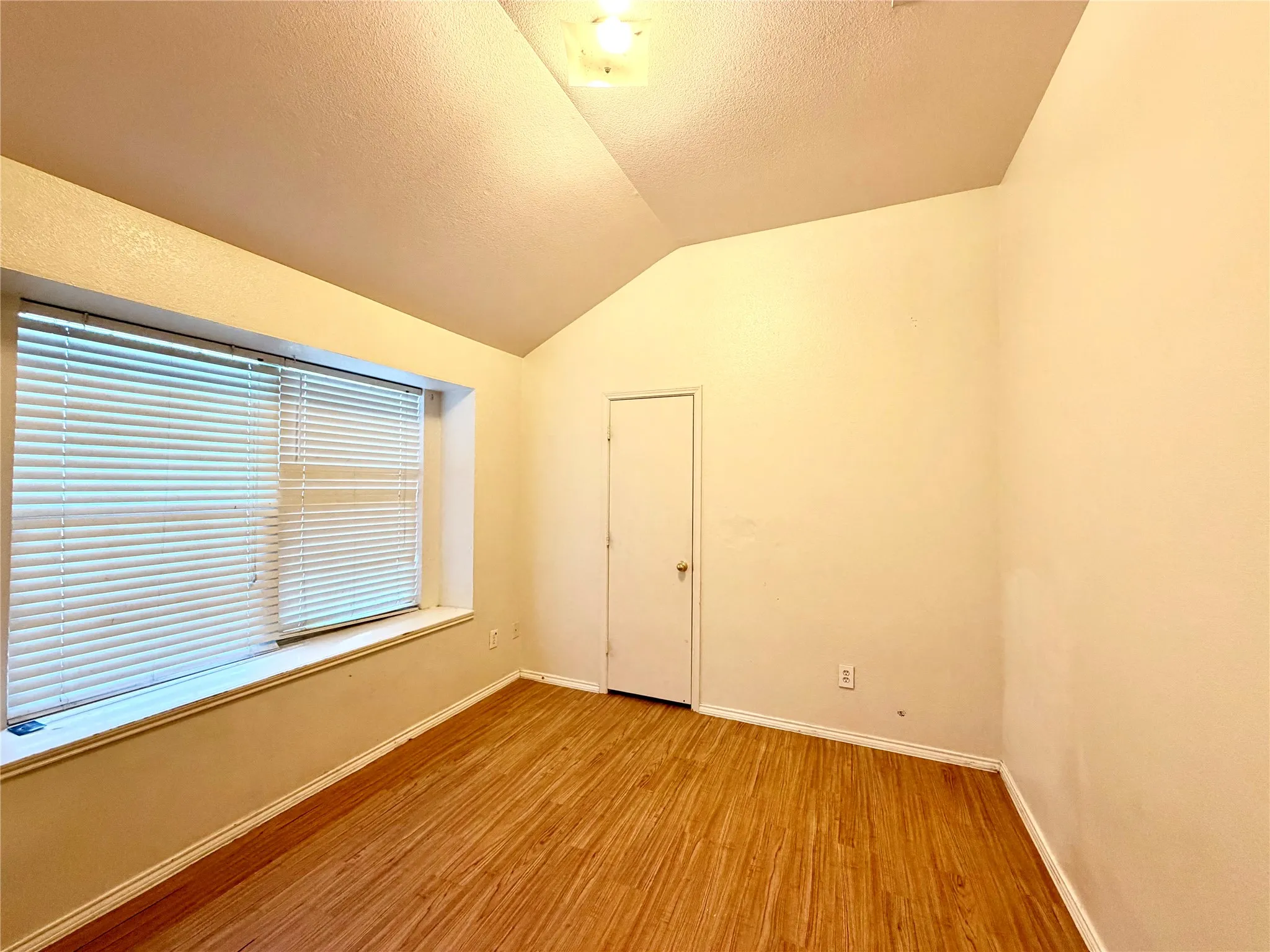 Vaulted ceiling with a flush-mount light fixture, wood-finish flooring, a window with blinds, and a built-in window bench
