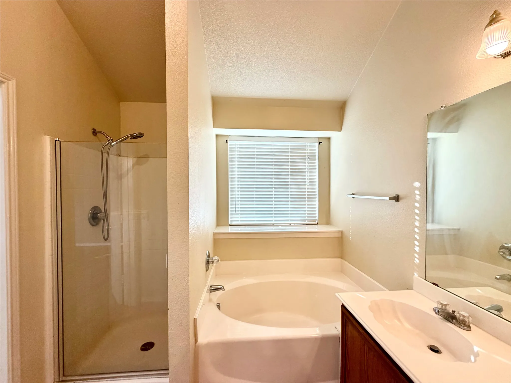 Built-in bathtub, separate shower enclosure with clear glass door, single vanity with wood-finish cabinetry, integrated sink, and wall-mounted mirror
