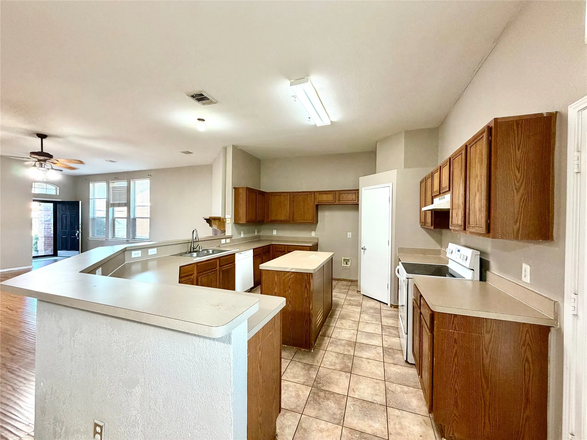 Kitchen featuring an expansive U-shaped countertop, wood-finish cabinetry, central island, and ceramic tile flooring