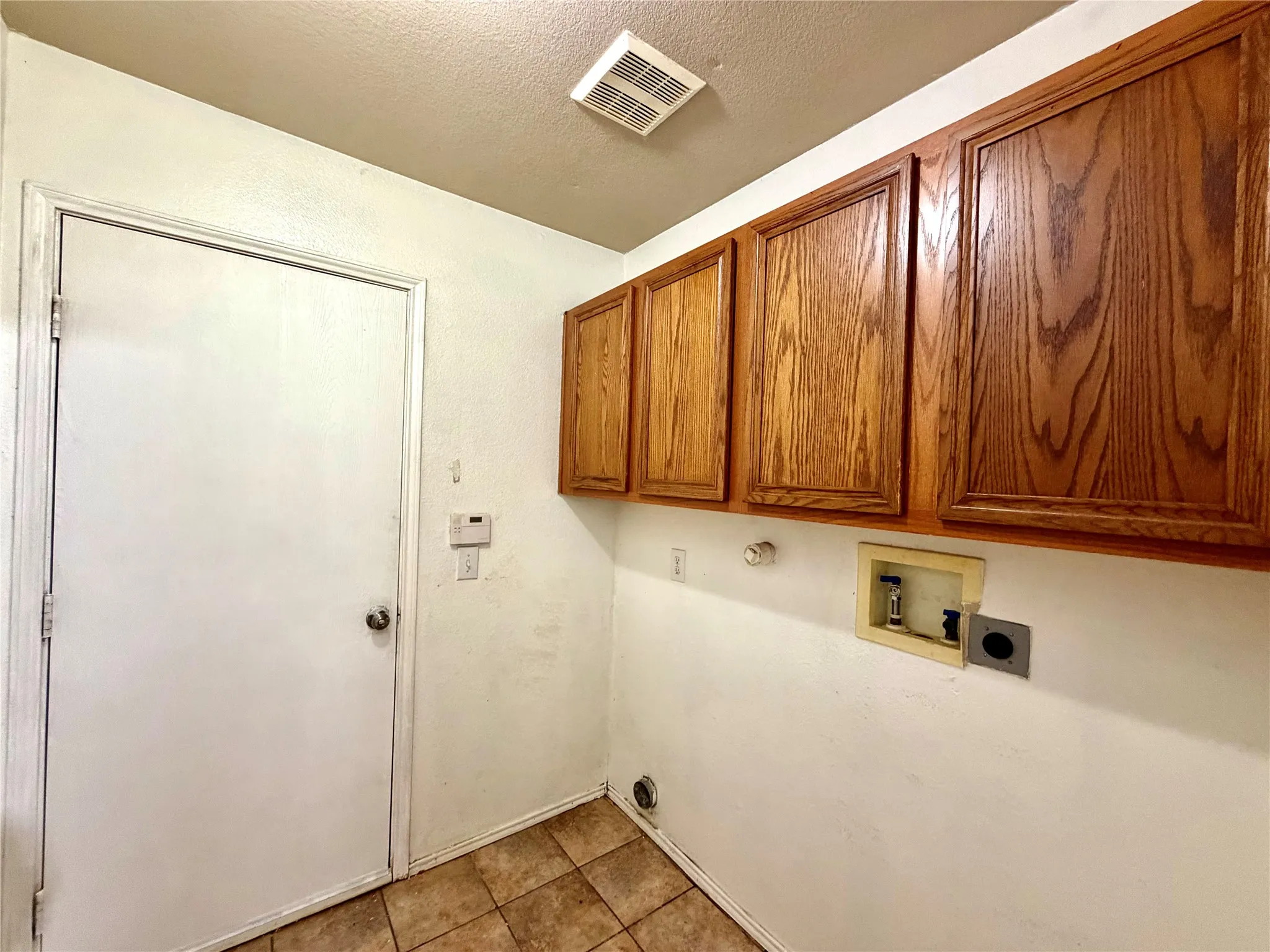 Overhead cabinetry with a wood finish, tile flooring, and utility hookups