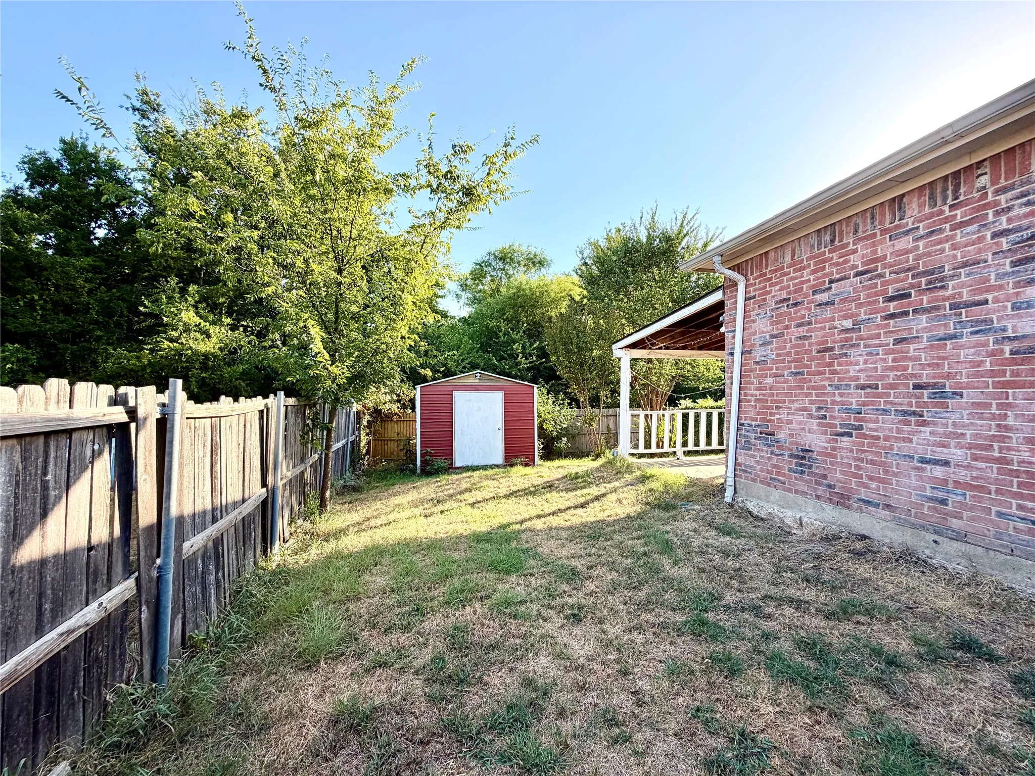 Brick exterior, covered patio with white railing, wood privacy fence, and red storage shed