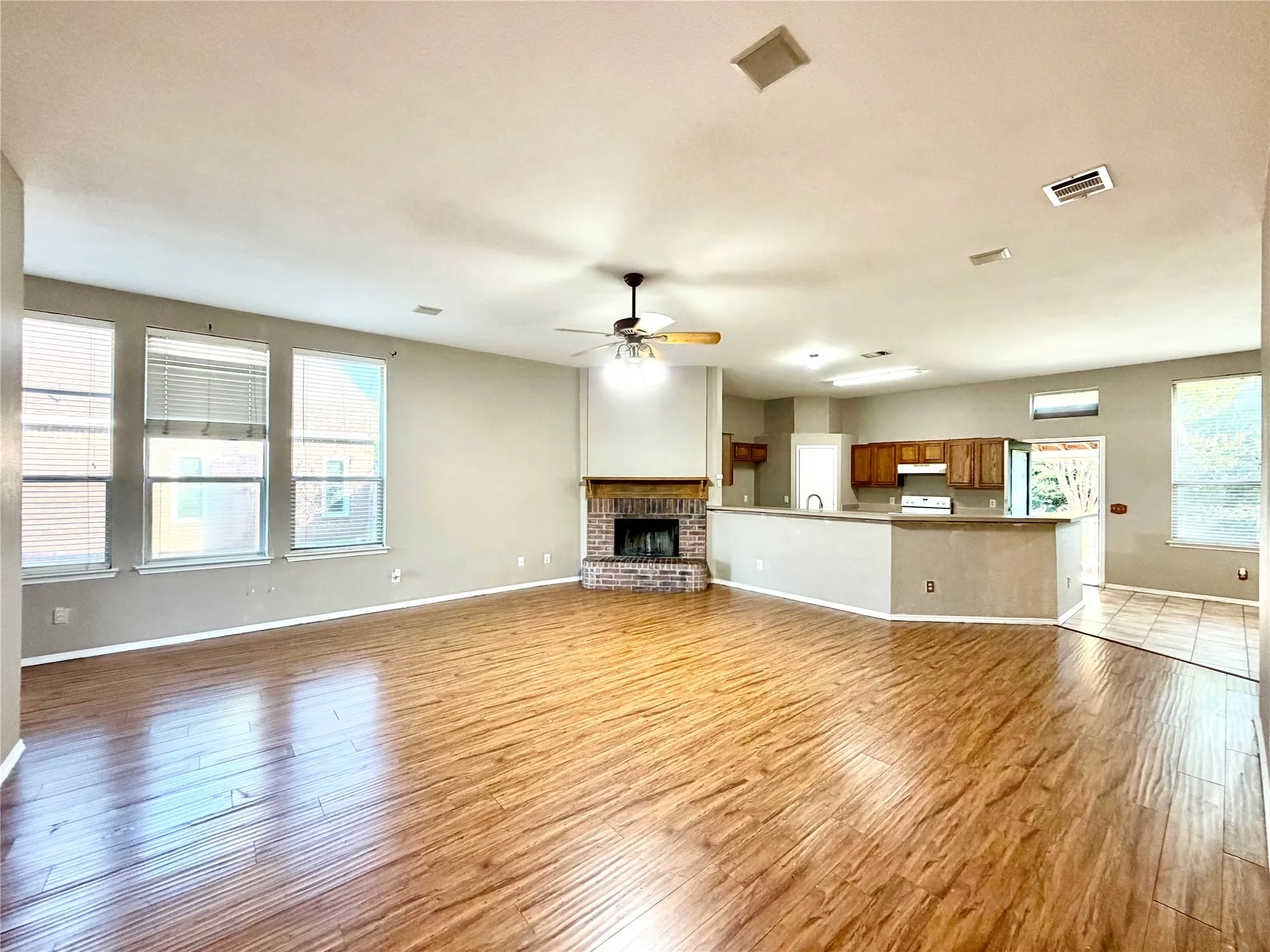 Spacious room featuring wood-finish flooring, a brick fireplace, and multiple windows
