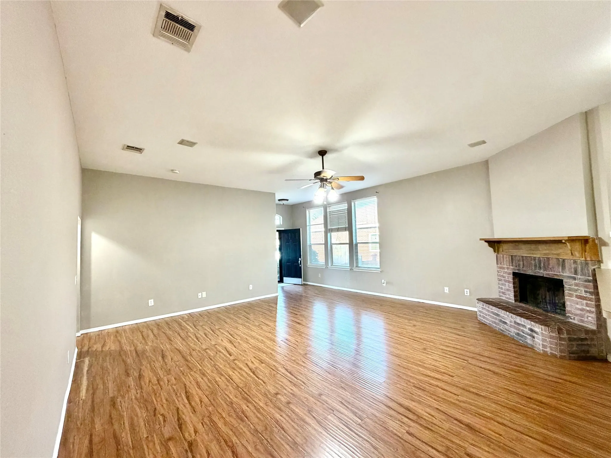 Wood-finish flooring, brick fireplace with a wood mantle, ceiling fan with integrated lighting, multiple windows, and a vaulted ceiling