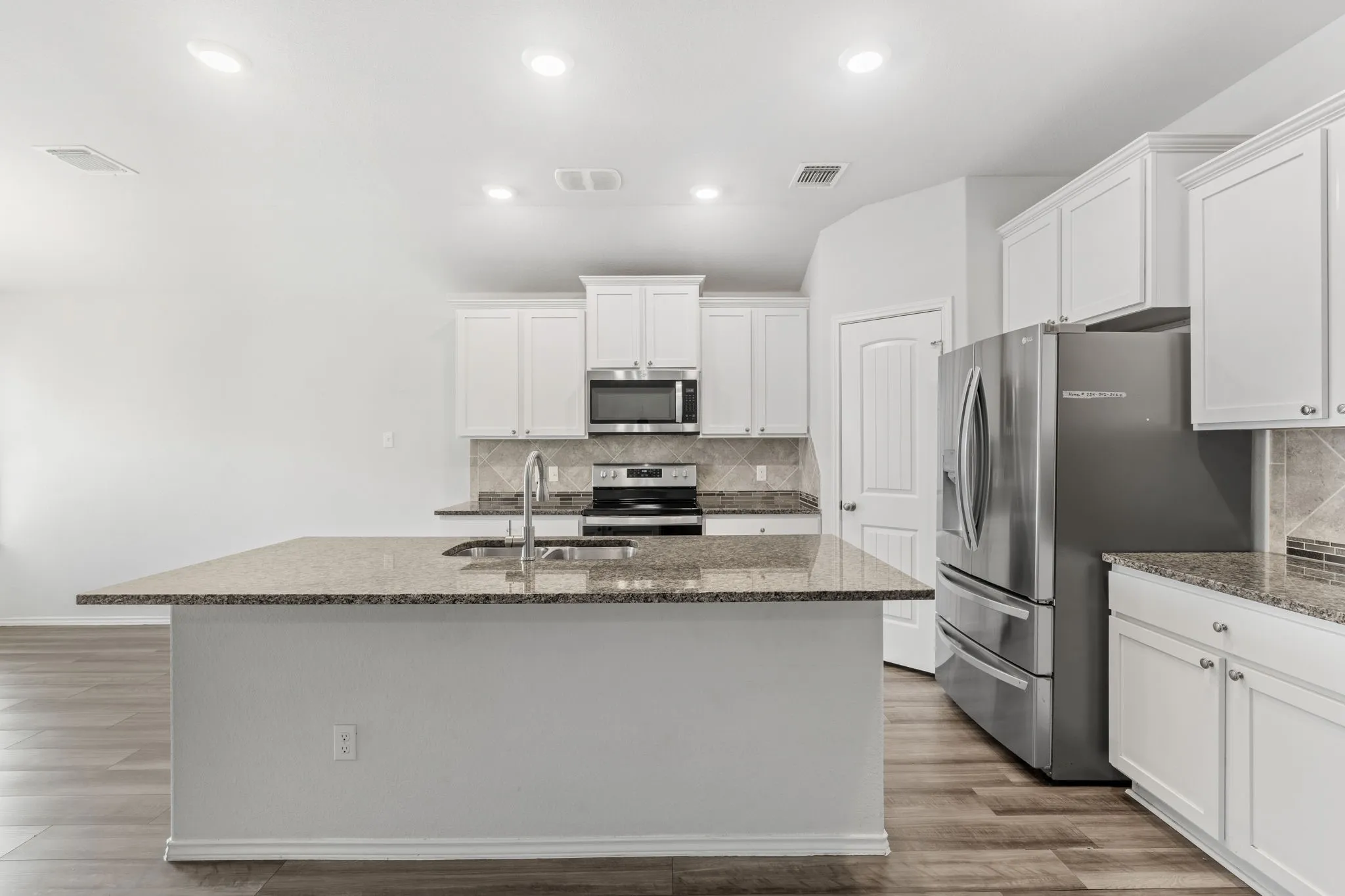 Contemporary kitchen featuring white cabinetry, granite countertops, stainless steel appliances, wood-finish flooring, and recessed lighting