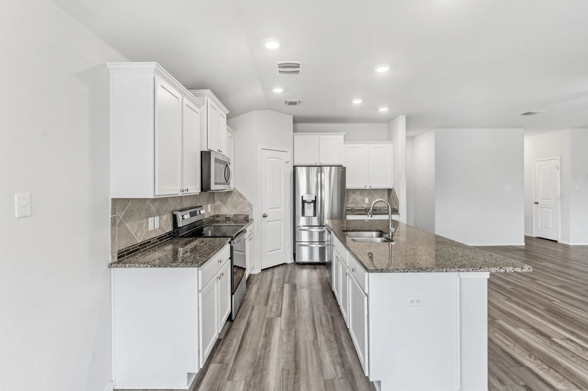 Kitchen featuring white cabinetry, stainless steel appliances, granite countertops, tile backsplash, and wood-finish flooring