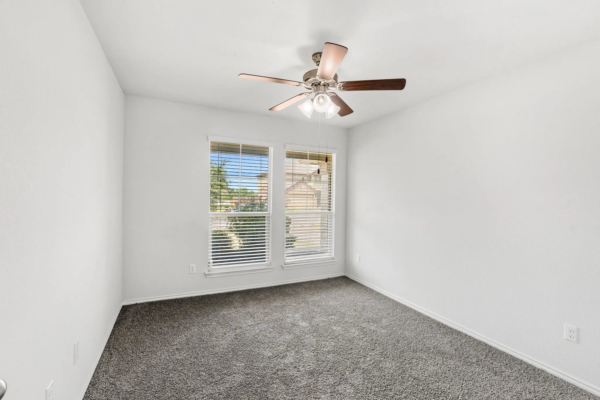 Dual windows with blinds, ceiling fan with light fixture, neutral wall finishes, and gray carpeting