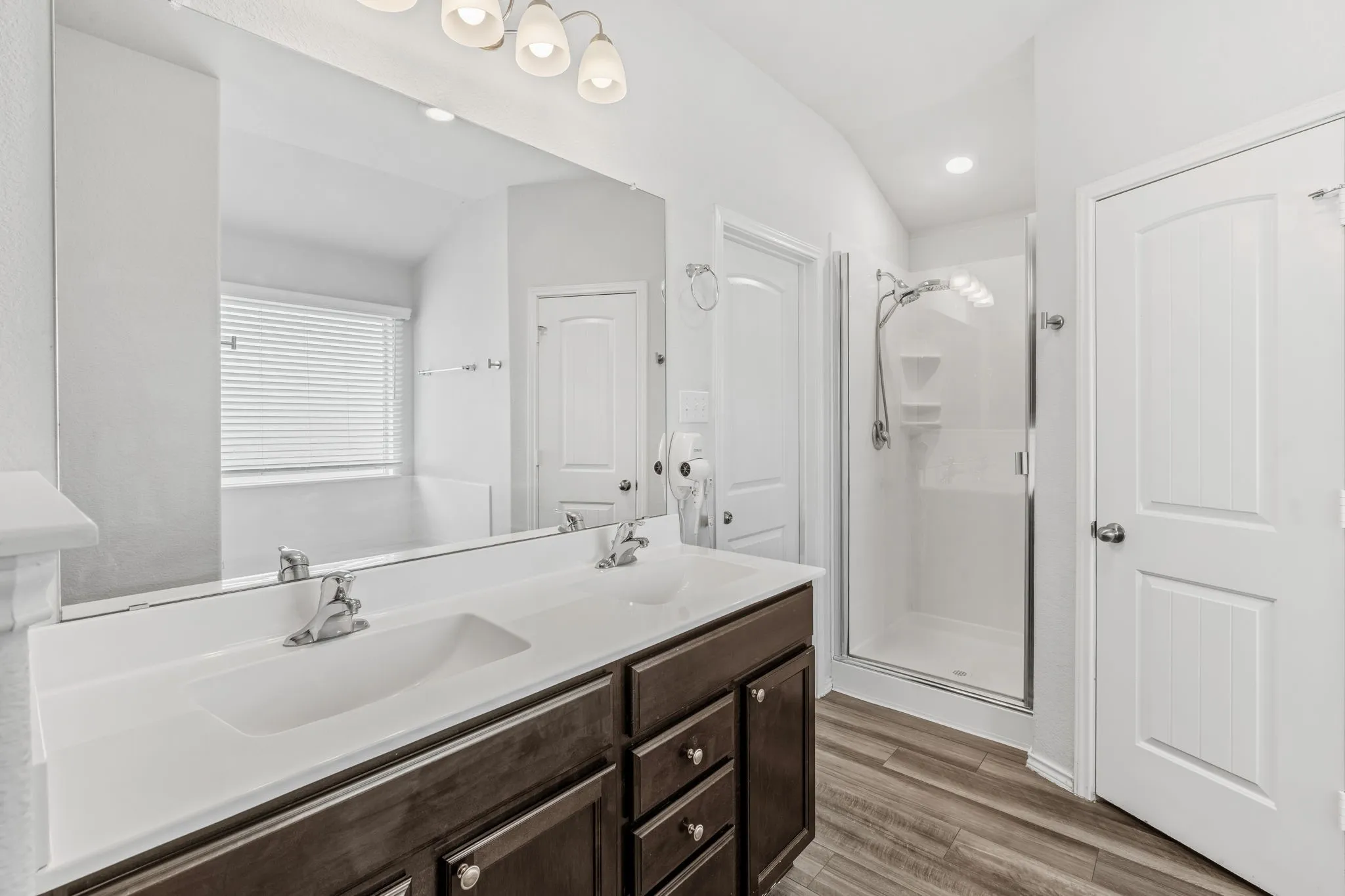 Dual vanity with undermount sinks, bronze wood-finish cabinetry, and a walk-in shower with clear glass enclosure