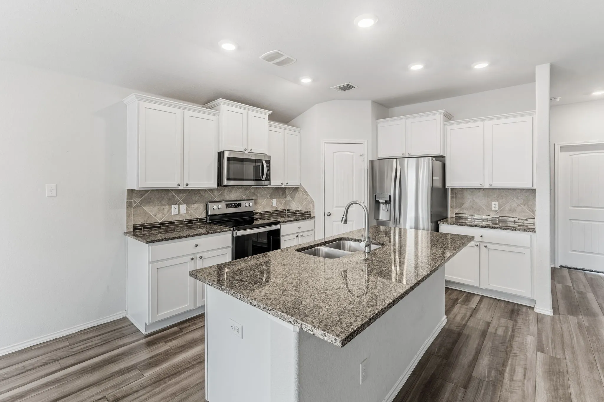 Kitchen featuring white shaker cabinetry, stainless steel appliances, speckled stone countertops, and wood-finish flooring