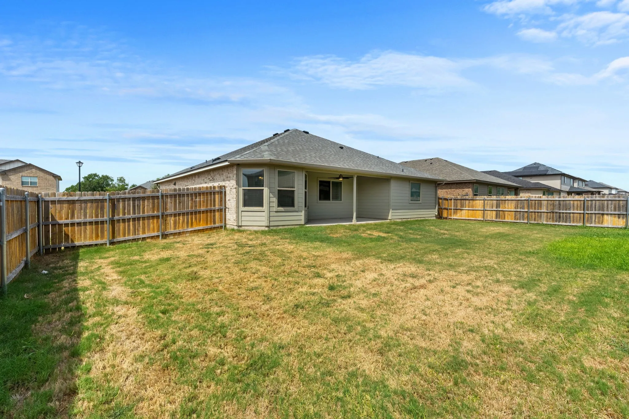 Expansive backyard with a full wood privacy fence, covered patio, and exterior lighting