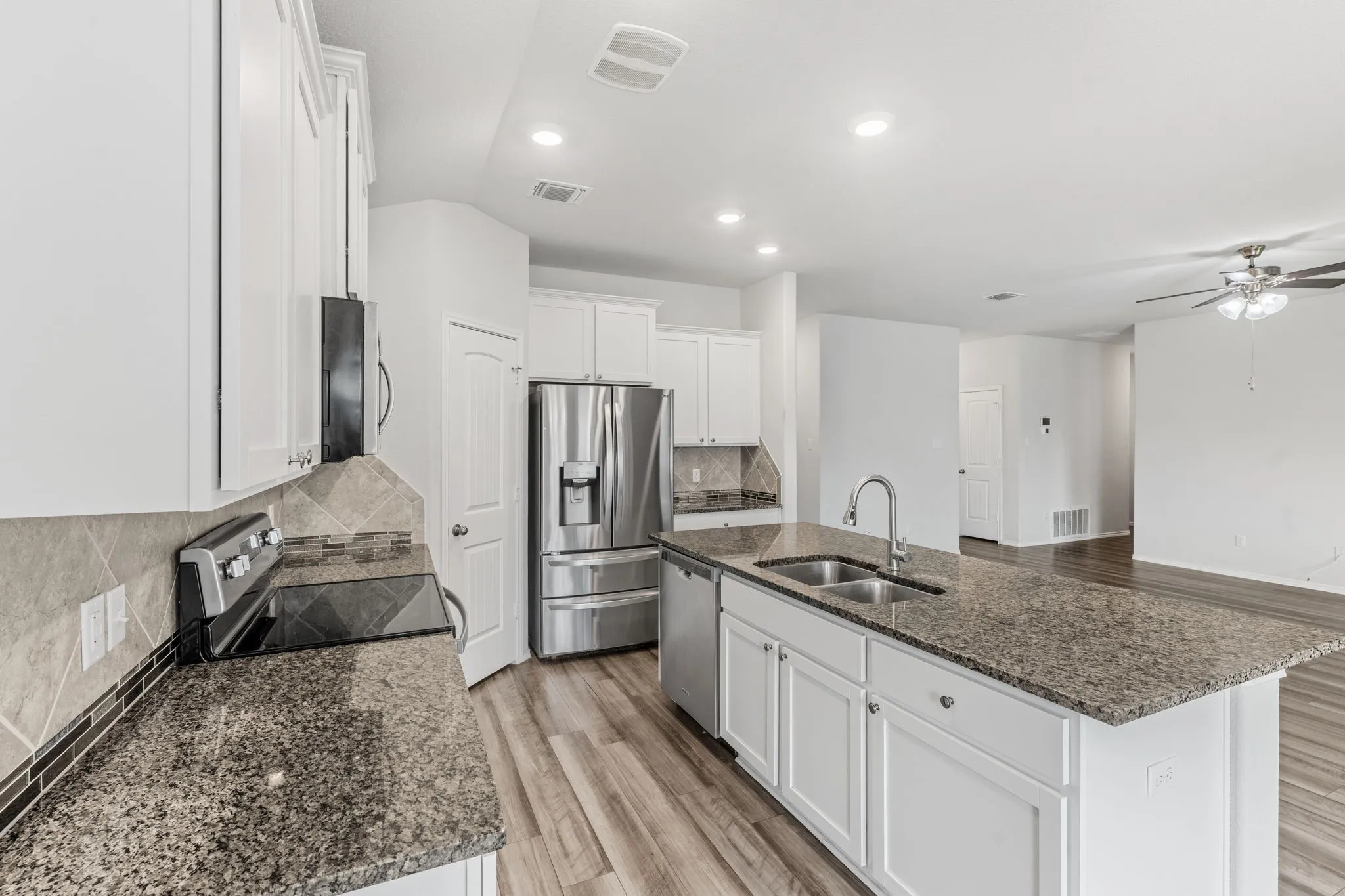 Kitchen featuring white cabinetry, stone countertops, stainless steel appliances, a large island with an integrated sink, and wood-finish flooring