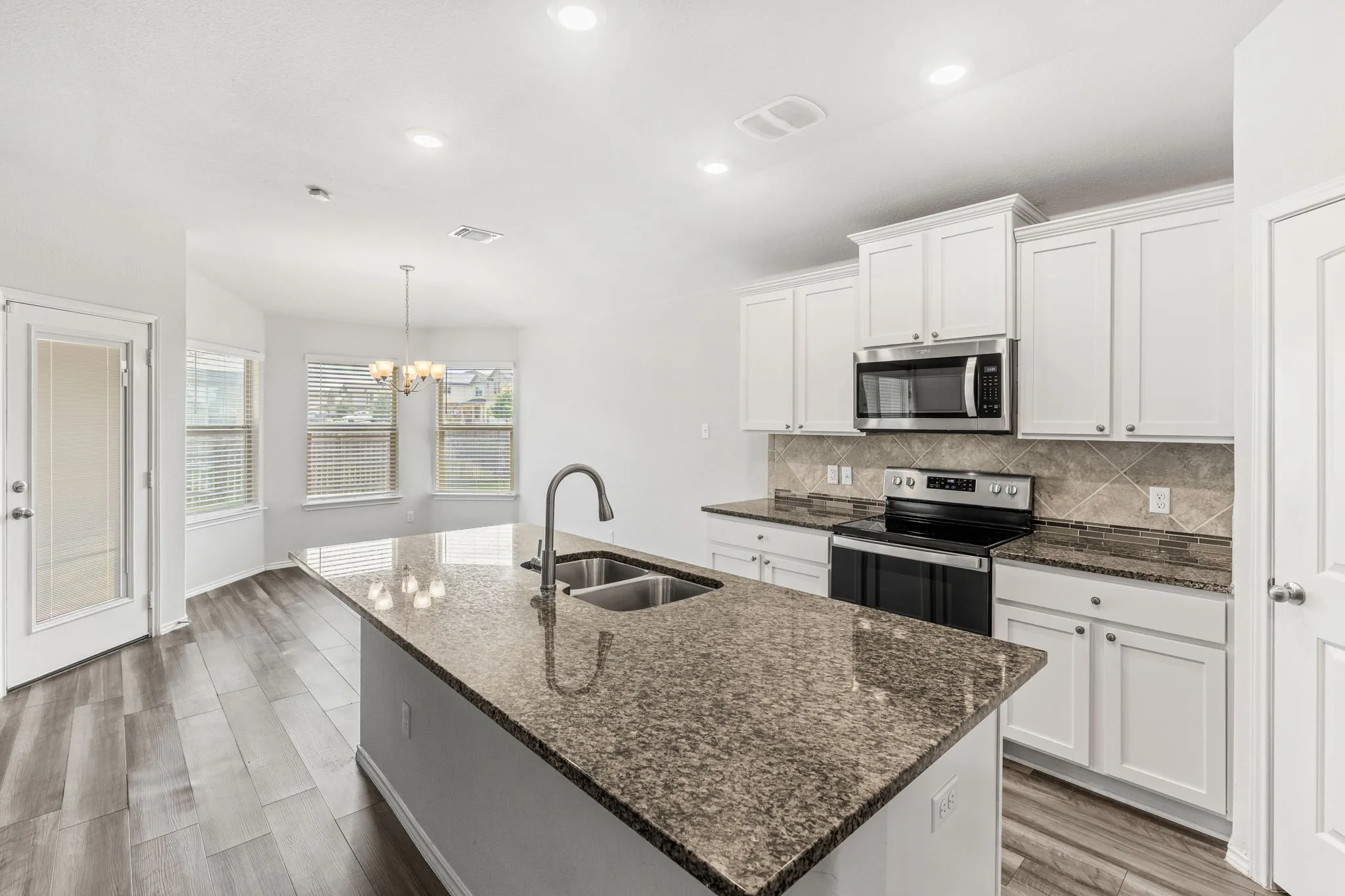 Kitchen with white cabinetry, stainless steel appliances, a large island with a double basin sink, and wood-finish flooring