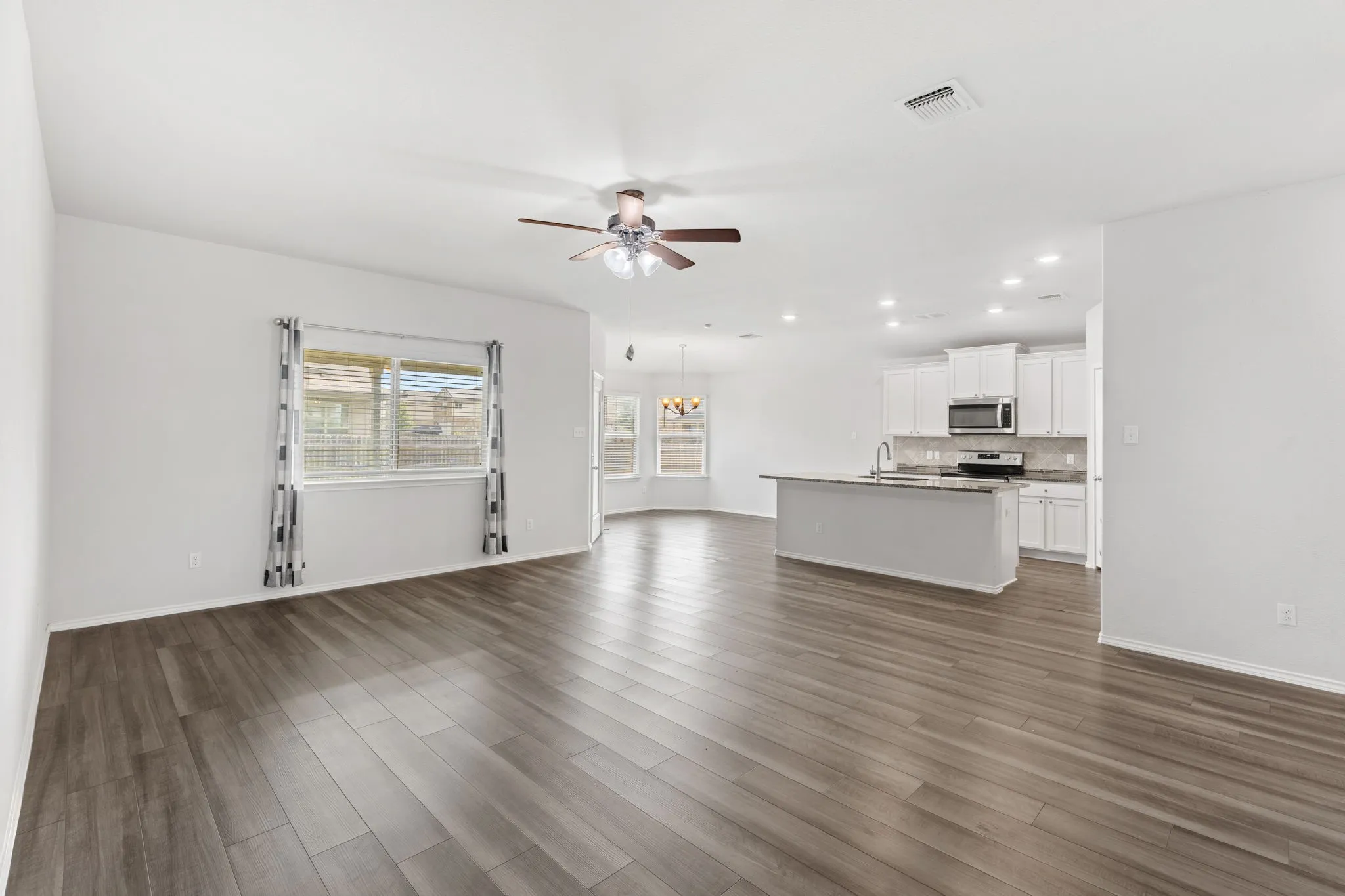 Open concept living area featuring wood-finish flooring, a kitchen island with sink, white cabinetry, and stainless steel appliances