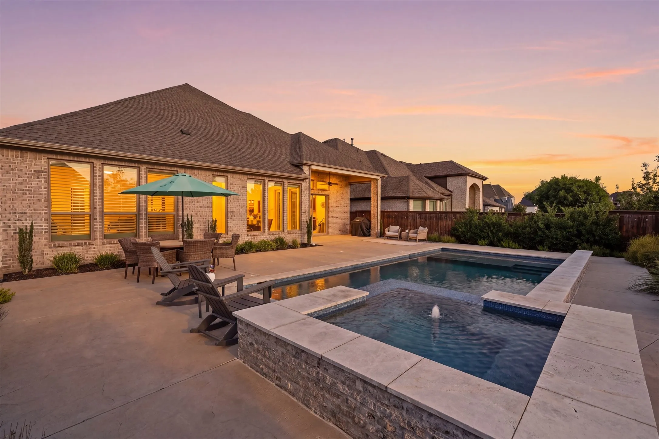Exterior brick facade with multiple windows, concrete patio, built-in swimming pool, and raised spa with water feature