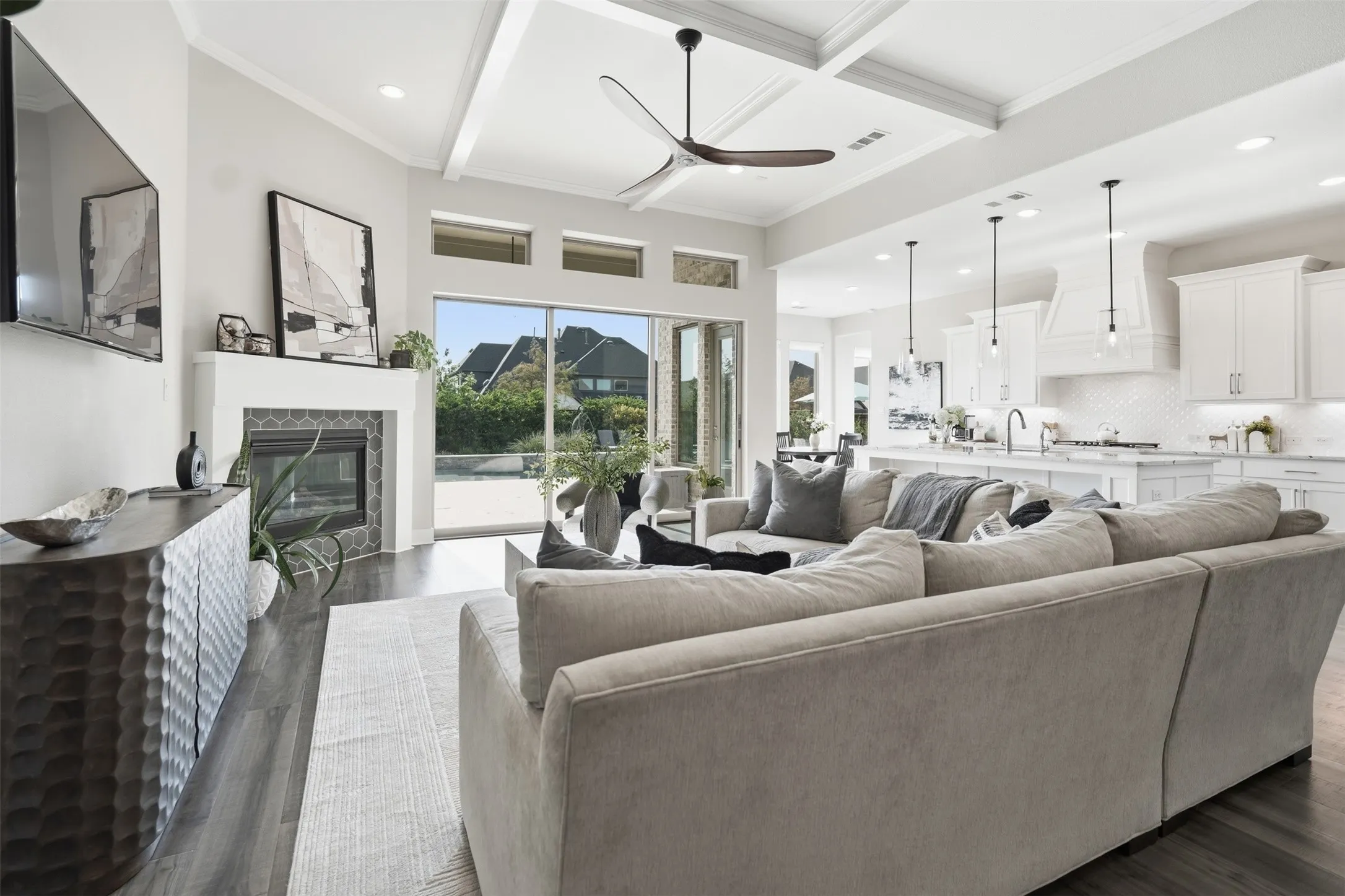 Open-concept living area with vaulted ceilings, exposed beams, a built-in fireplace featuring a geometric tile surround, wood-finish flooring, and a contemporary ceiling fan