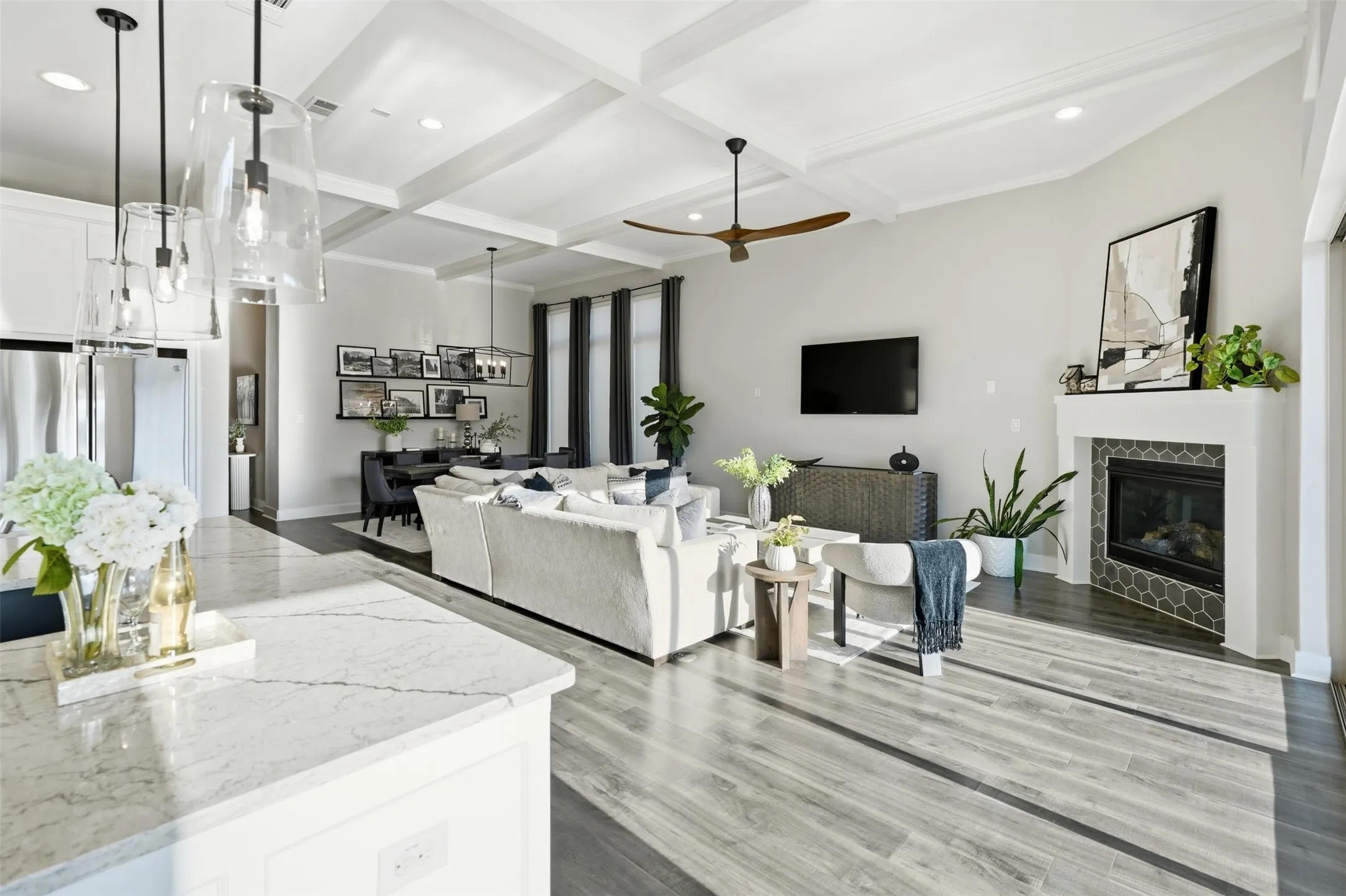 Open-concept living area with wood-finish flooring, a fireplace featuring hexagonal tile, and a coffered ceiling