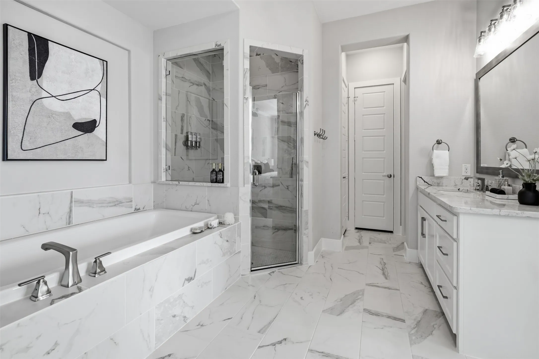 Soaking tub with deck-mounted fixtures, walk-in glass shower enclosure, white vanity with integrated sink, wall-mounted mirror, and marble-look tile flooring