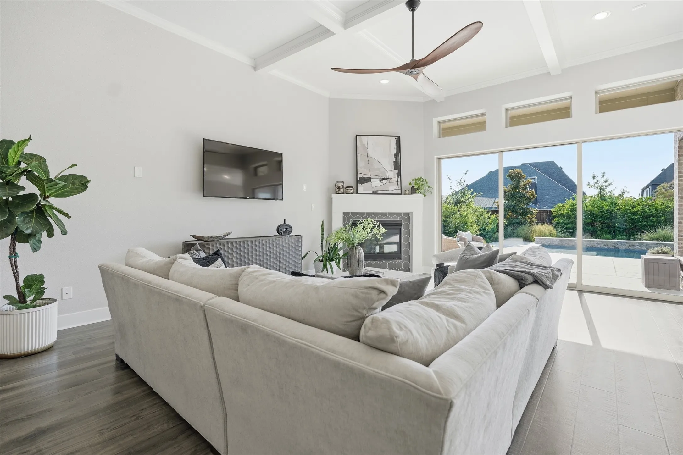 Wood-finish flooring, fireplace with tile surround, coffered ceiling, ceiling fan, and large sliding glass door