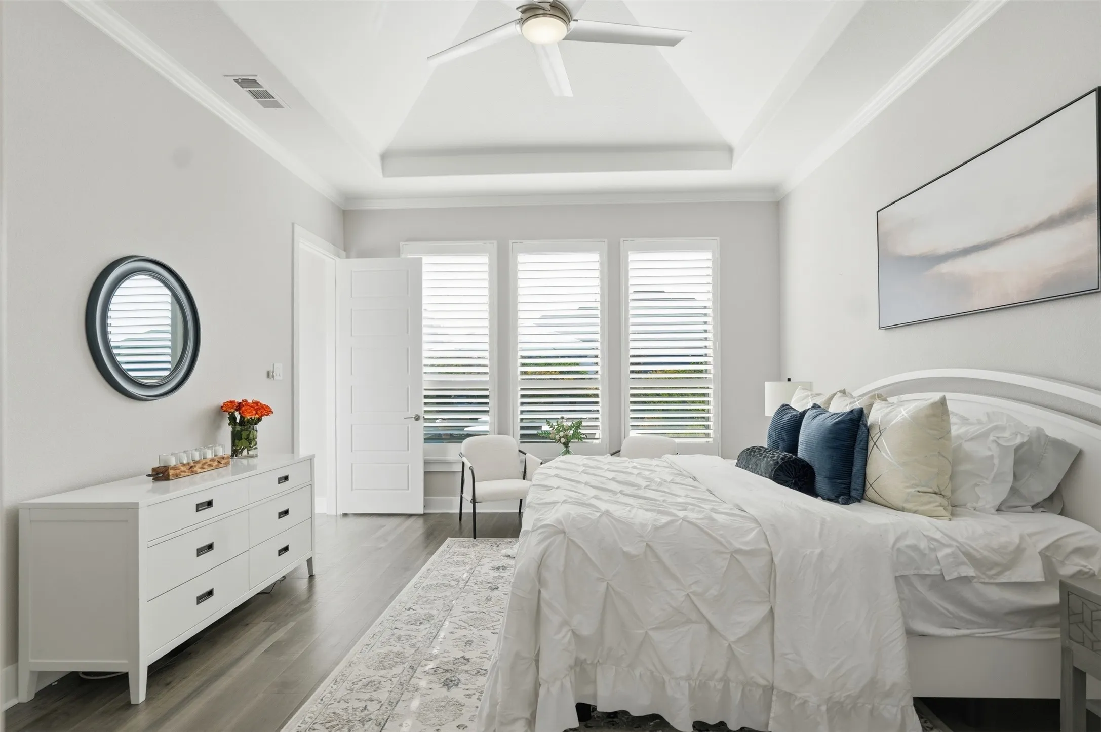 Vaulted ceiling with a flush-mount ceiling fan, crown molding, wood-finish flooring, and plantation shutters