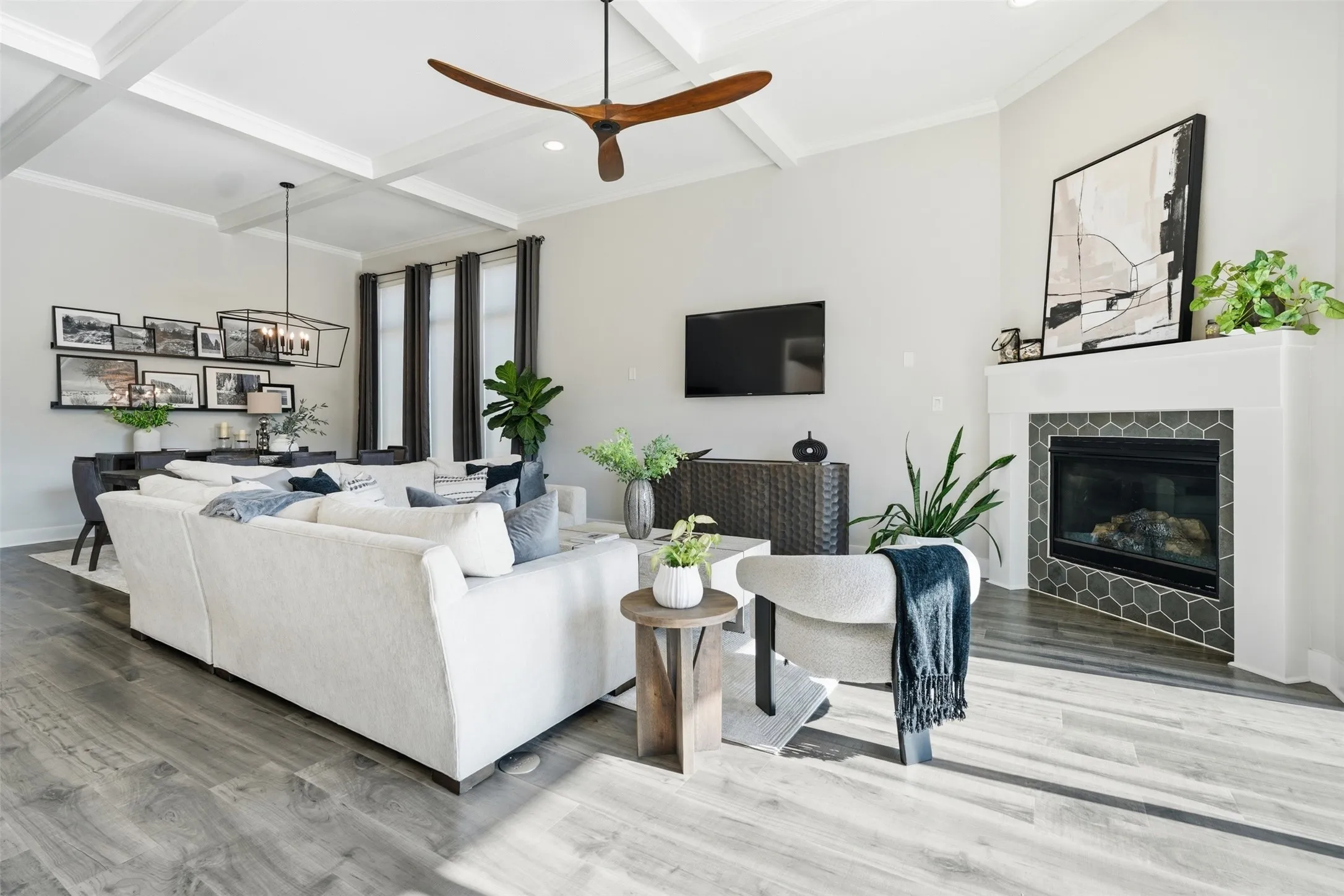 Vaulted ceiling with exposed beams, wood-finish flooring, fireplace with hexagonal tile surround, and tall windows with dark trim