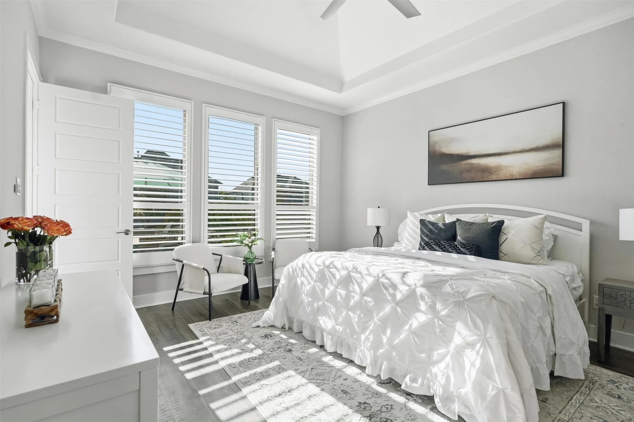 Tray ceiling with crown molding, wood-finish flooring, white plantation shutters, and a five-panel interior door