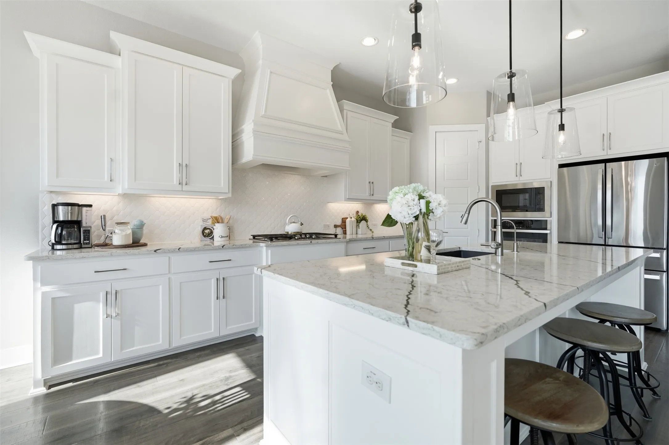 Kitchen featuring white cabinetry, light-toned countertops, a built-in kitchen island with seating, a stainless steel refrigerator, and pendant lighting