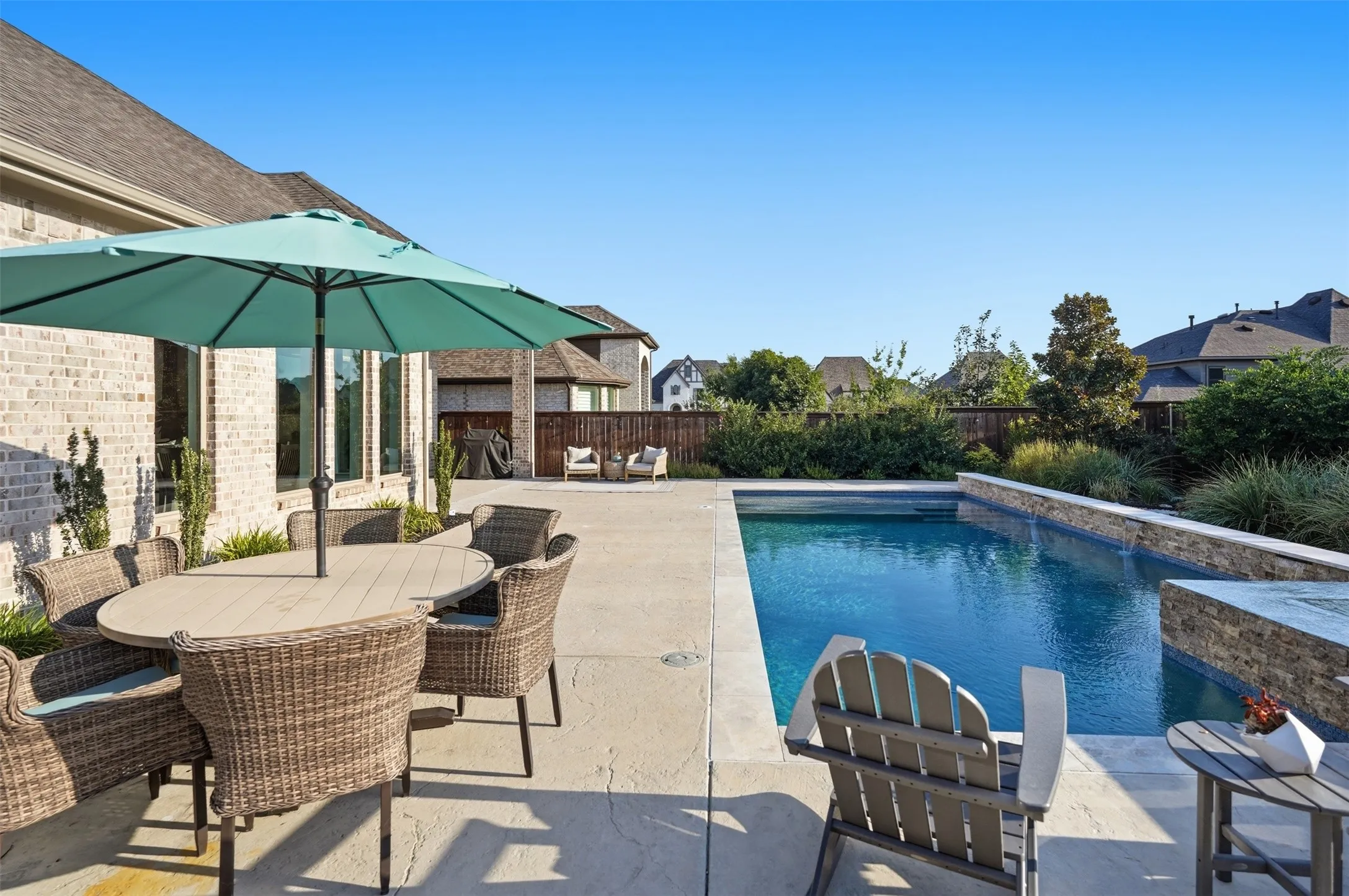 Backyard oasis featuring a rectangular swimming pool with stone-clad retaining walls, an expansive concrete patio, and mature perimeter landscaping