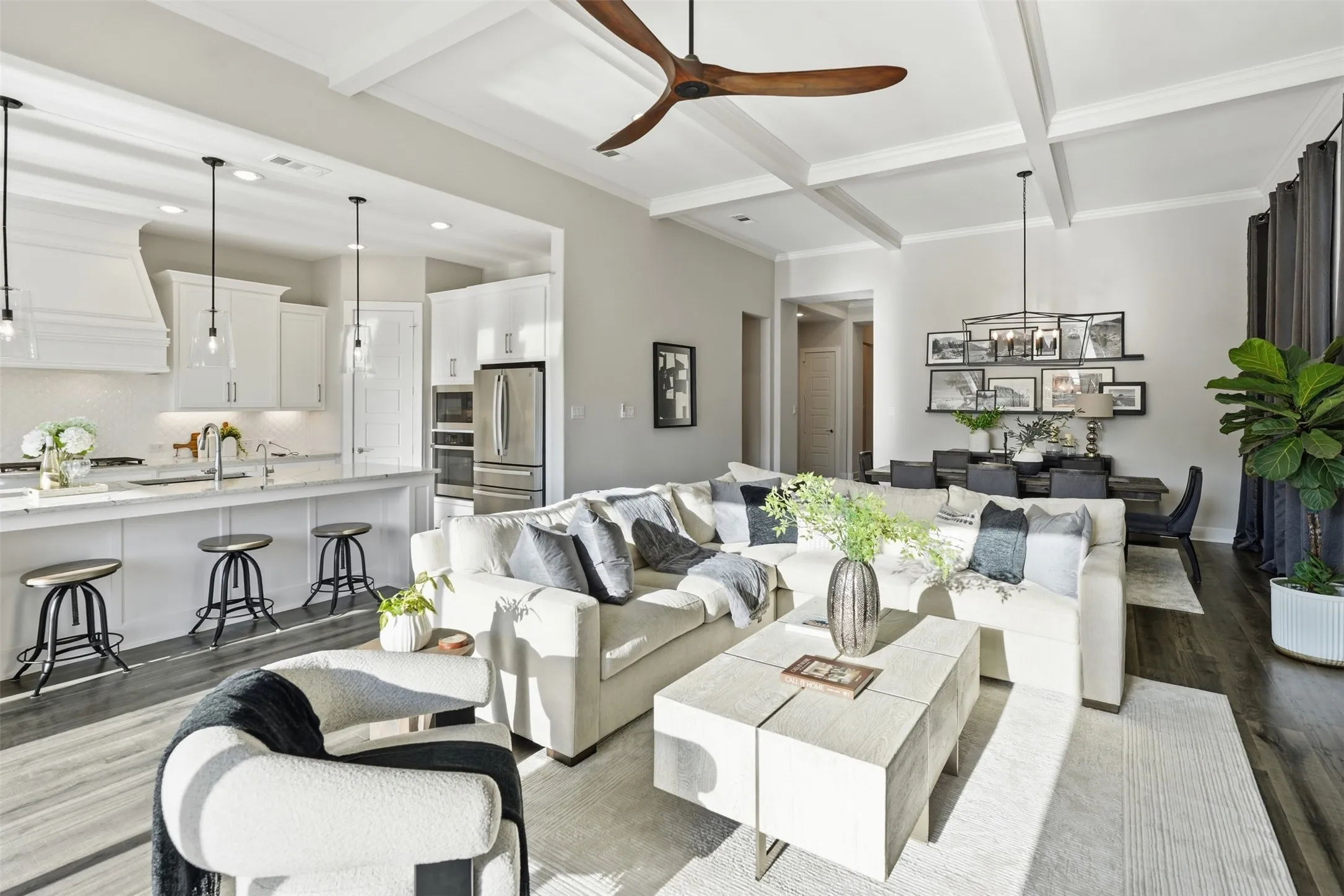 Open-concept living space featuring wood-finish flooring, coffered ceiling, and a kitchen island with pendant lighting