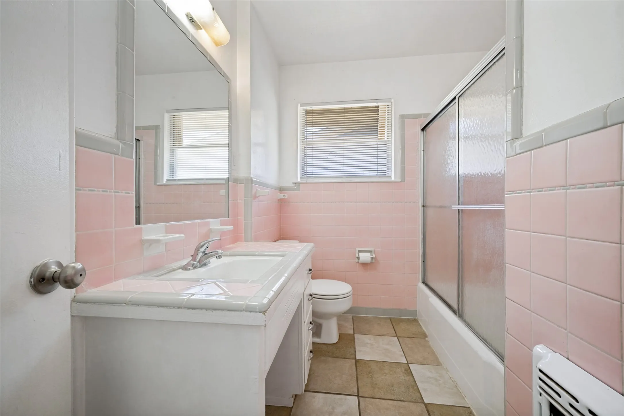 Bathroom featuring pink ceramic wall tiles, a vanity with an integrated sink, a built-in mirror, a sliding glass shower enclosure, and checkerboard floor tiles