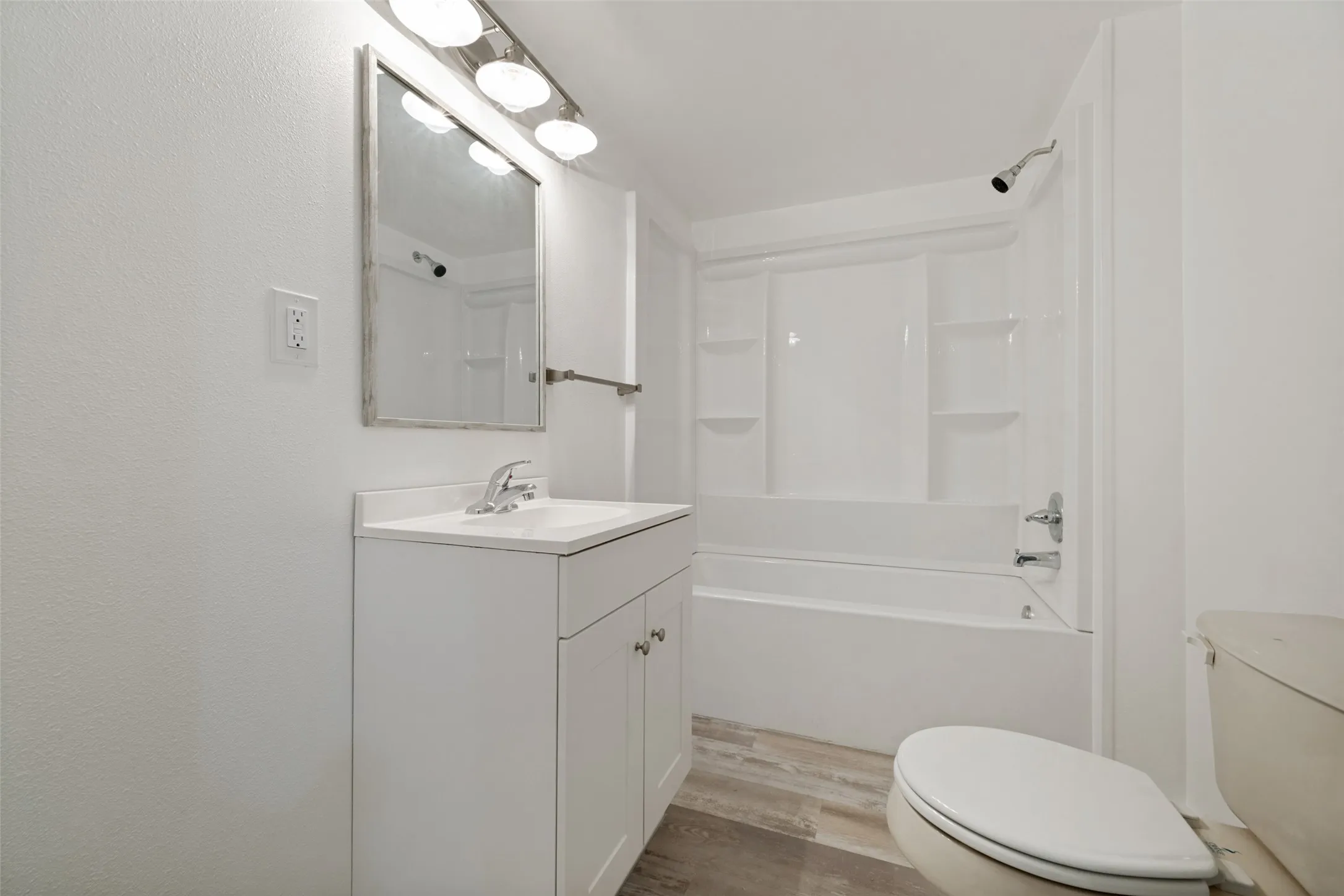 White vanity with integrated sink, chrome faucet, and overhead bar lighting