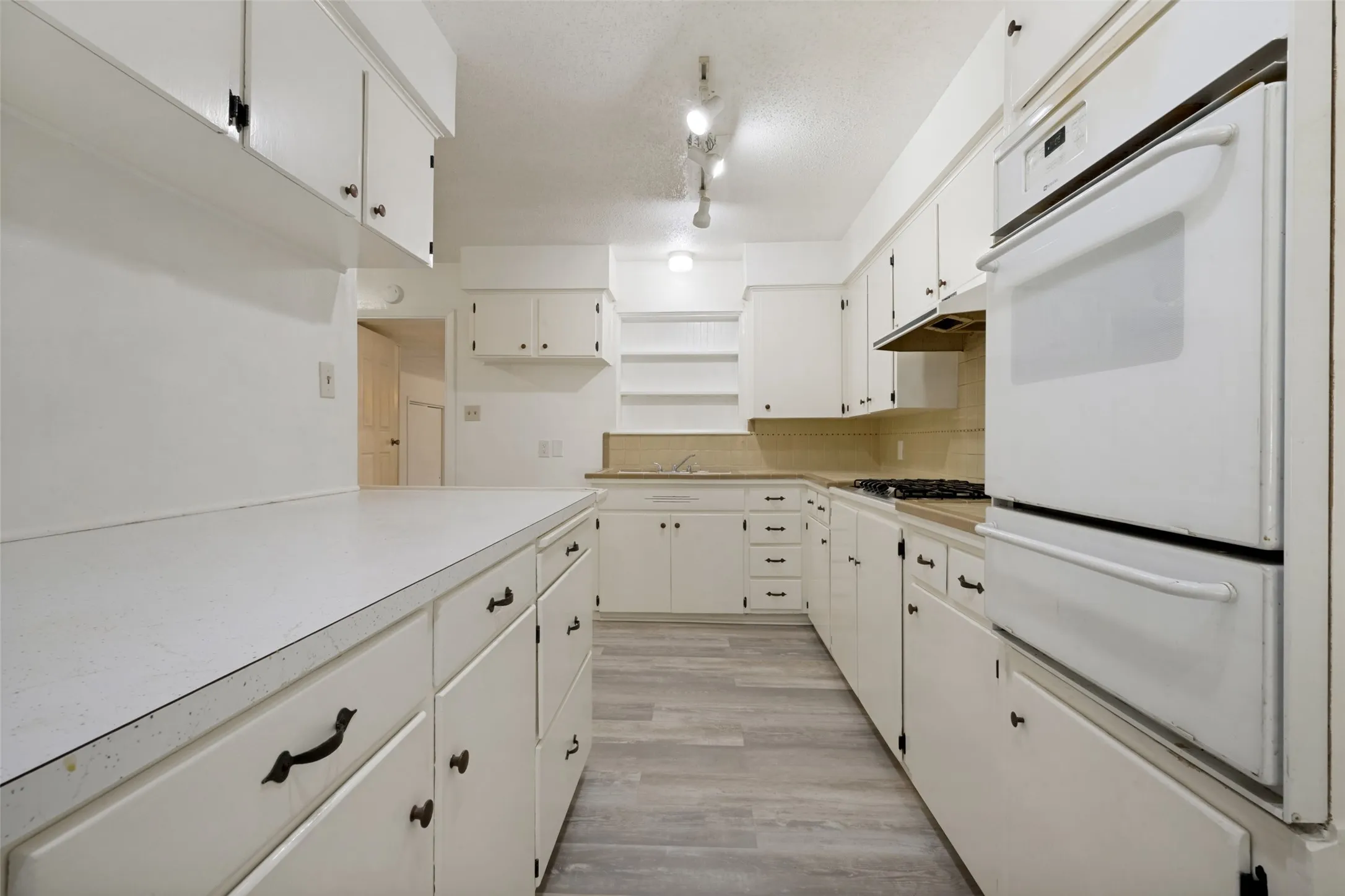 Kitchen featuring white cabinetry, light-toned countertops, wood-finish flooring, a built-in oven, and a gas cooktop