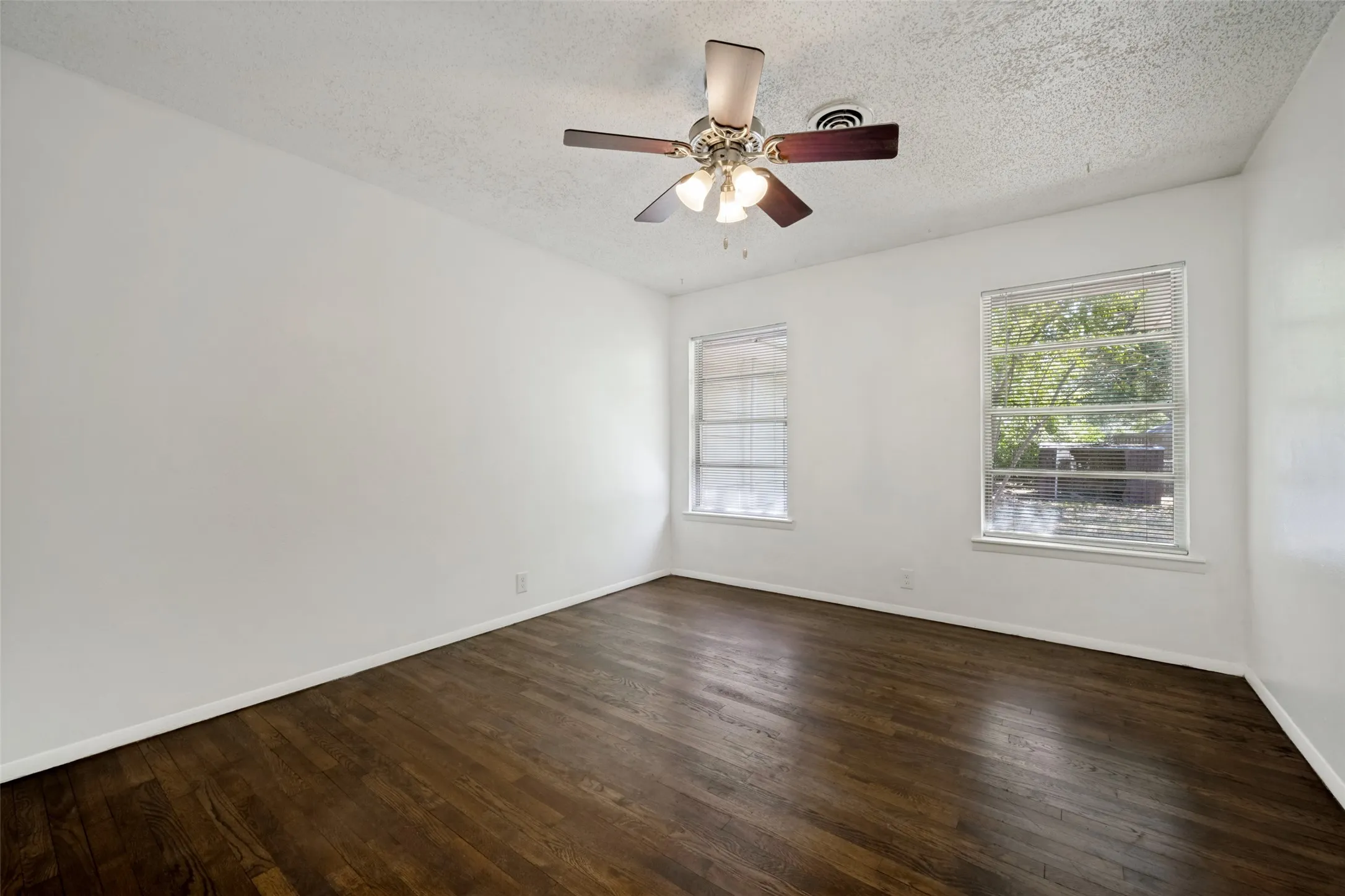 Hardwood flooring, two windows, ceiling fan with light fixture, and white walls