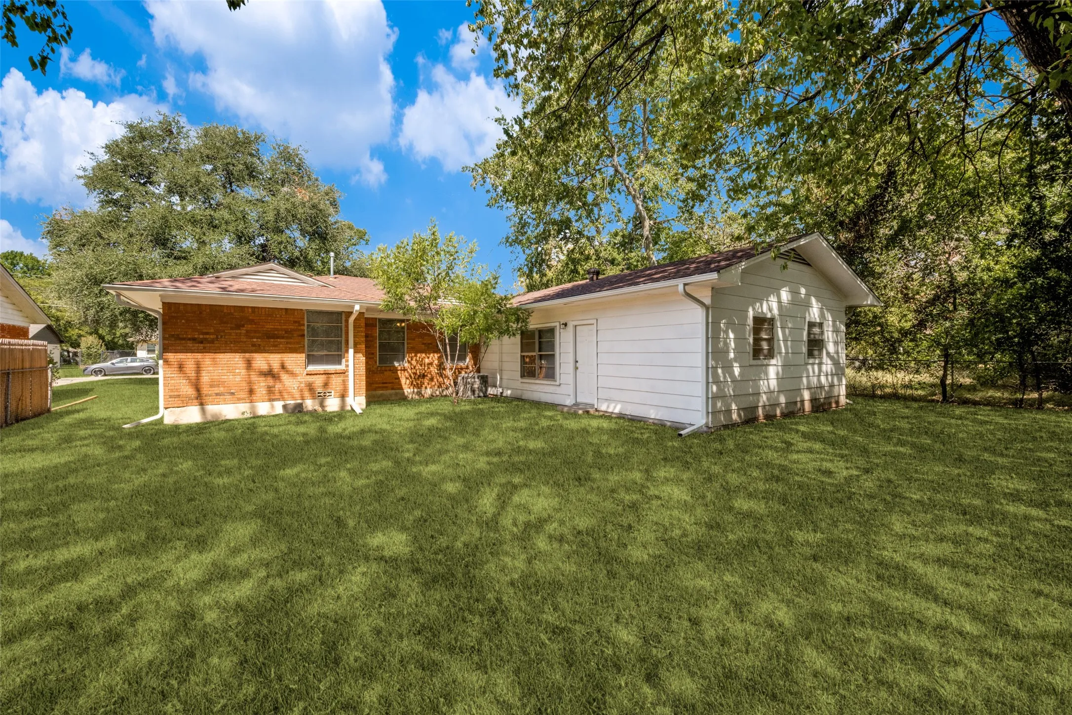 Expansive green lawn with mature trees, brick exterior, and a detached structure with siding