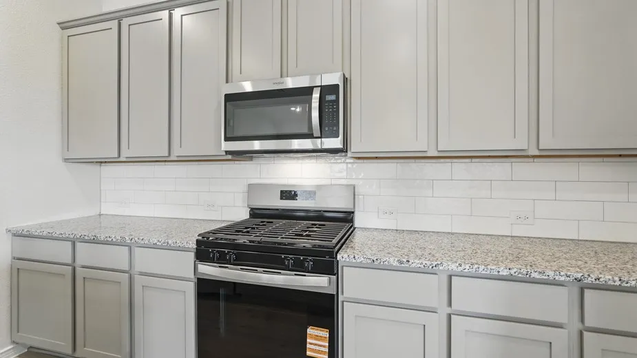 Kitchen featuring light grey cabinetry, stainless steel microwave, gas range, white subway tile backsplash, and speckled countertops