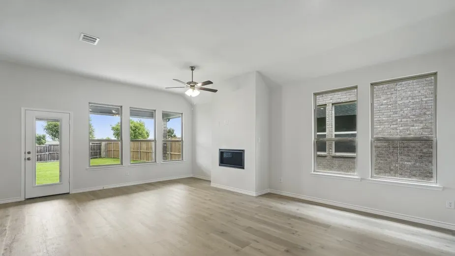 Spacious room featuring light wood-finish flooring, a modern electric fireplace, a ceiling fan with integrated lighting, and multiple windows