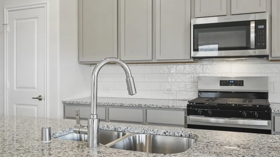 Granite countertops, stainless steel sink, chrome gooseneck faucet, light gray cabinetry, and white subway tile backsplash