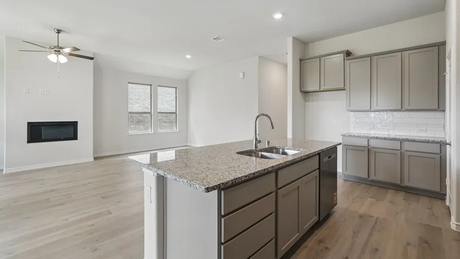 Wood-finish flooring throughout, kitchen island with built-in sink and granite countertop, gray cabinetry, subway tile backsplash, and an electric fireplace
