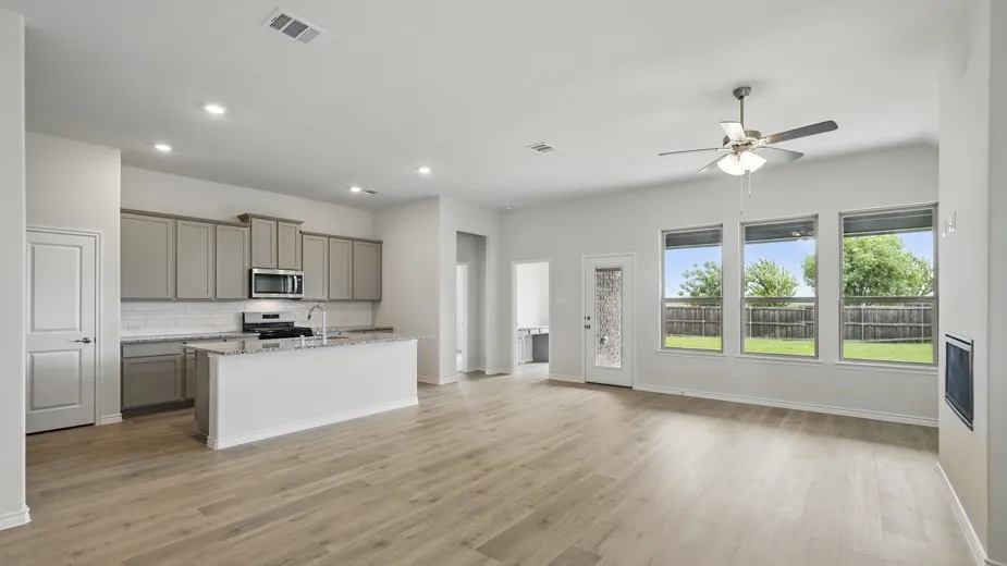Open-concept living space featuring wood-finish flooring, a kitchen island with granite countertop, stainless steel appliances, and a ceiling fan
