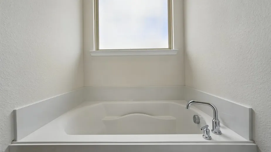 Built-in soaking tub with deck-mounted chrome fixtures, integrated armrests, and a frosted privacy window