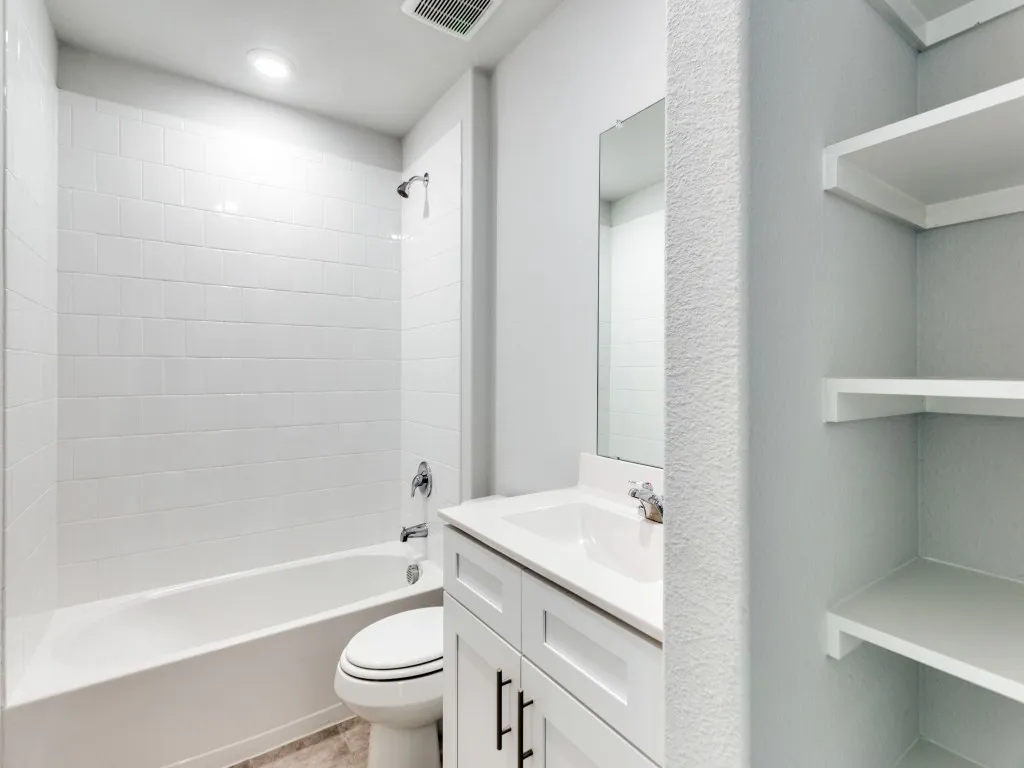 Bathroom featuring a white subway tile shower surround, a white vanity with an integrated sink, a chrome faucet, and built-in shelving