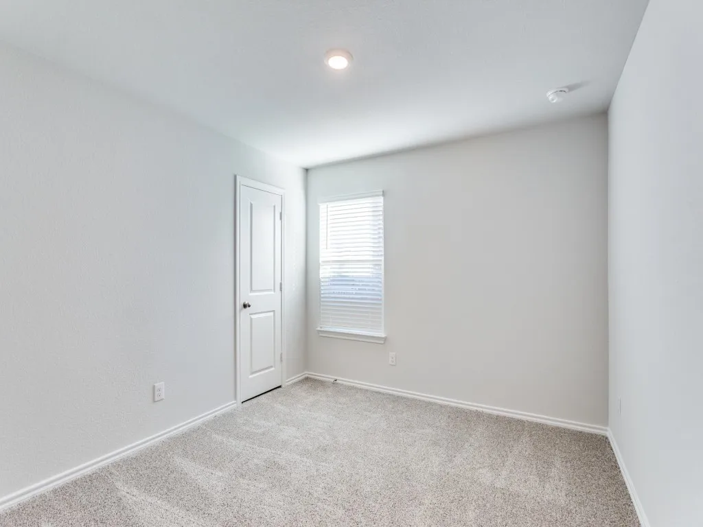 Neutral-toned carpeting with white baseboards, a white paneled door, and a single window with blinds